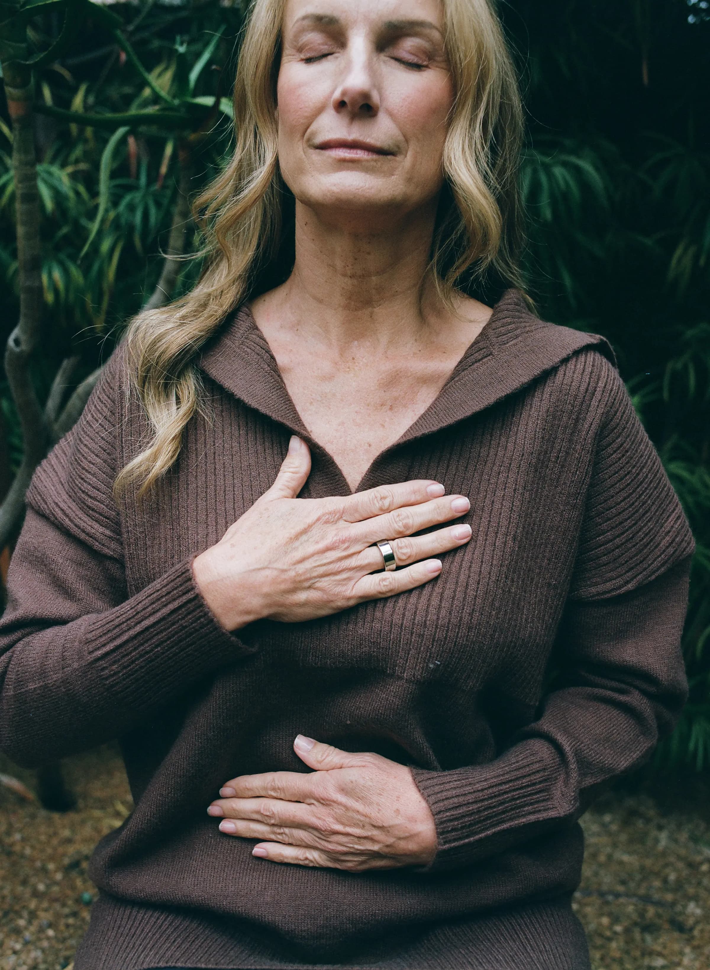 Woman wearing a brown sweater with her right hand pressed against her chest wearing an AlterMe ring